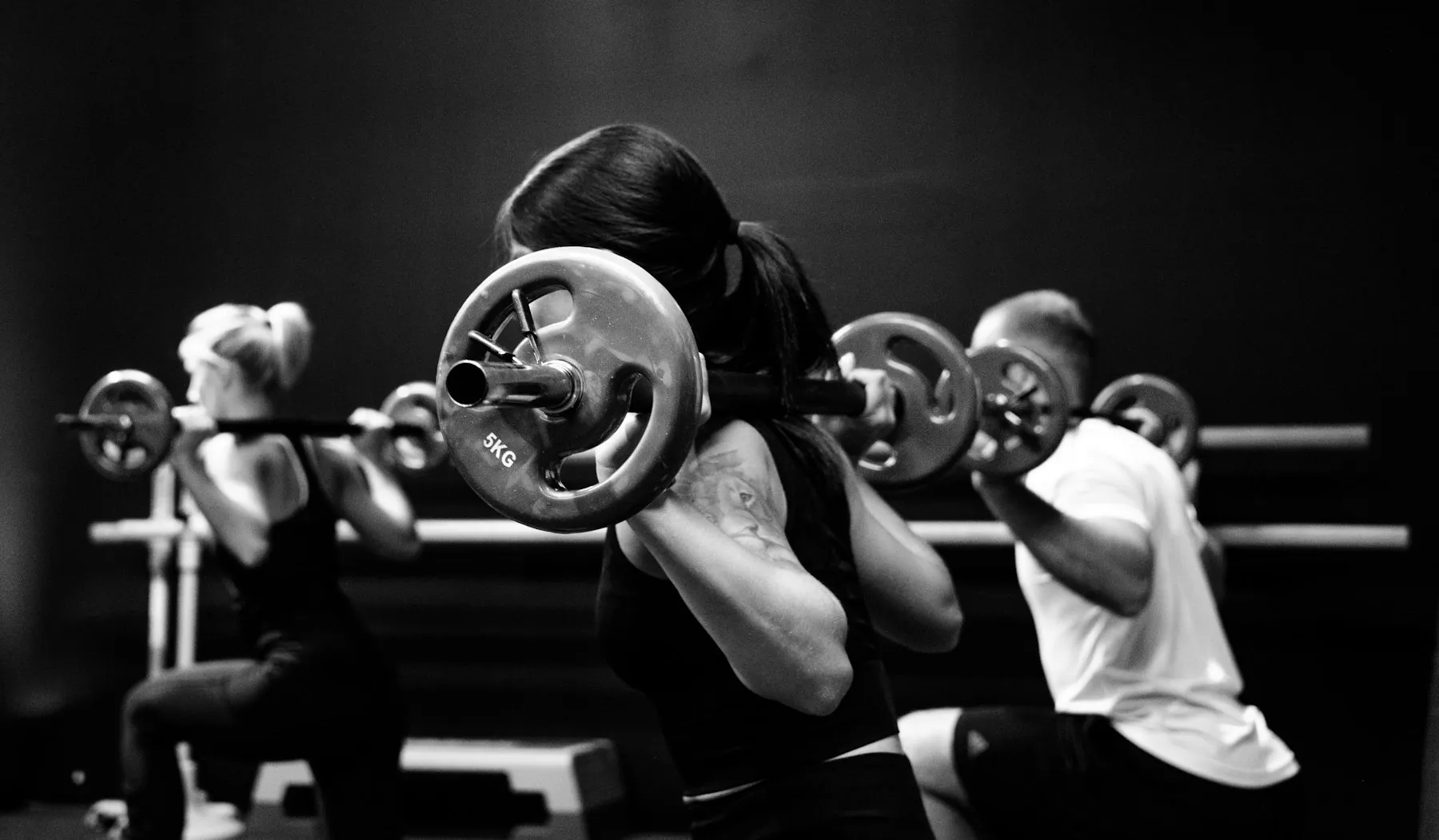 Three lifters in a row, squatting heavy barbells in a black and white gym photo