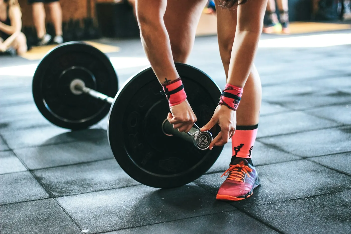A lifter loading a weight plate onto a barbell on a rubber gym floor