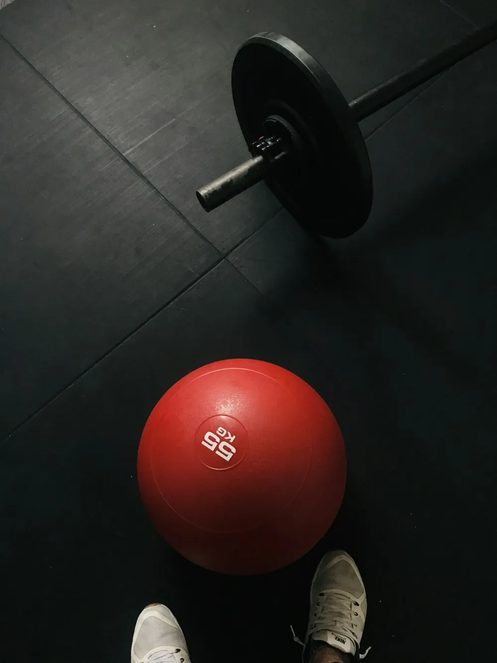 A red slam ball resting on black gym flooring next to a barbell plate